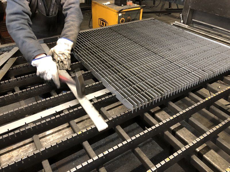 Un operaio, indossando i guanti, solleva una griglia metallica su un nastro trasportatore industriale.