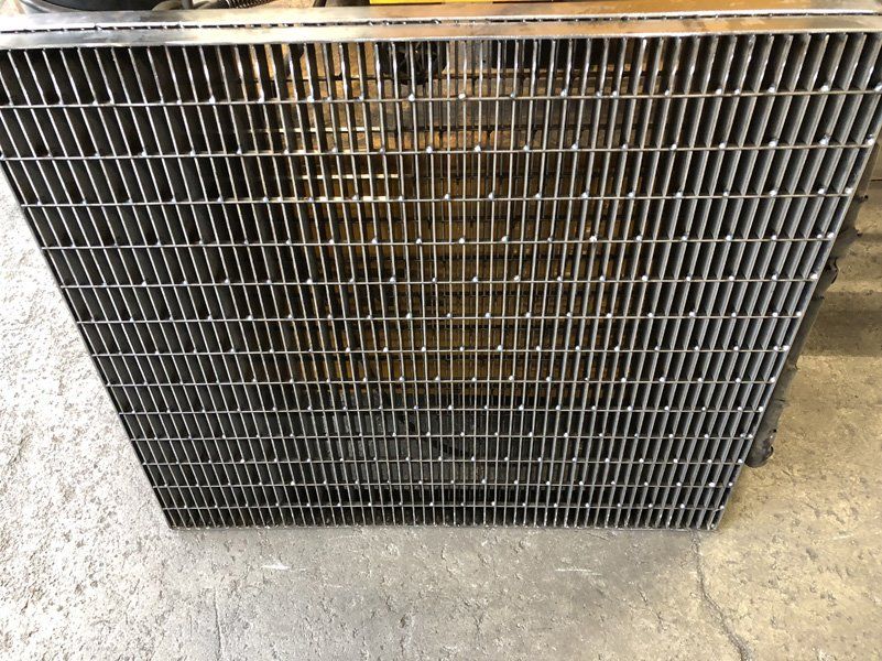 Primo piano di una serpentina di un radiatore o di un condensatore metallico sporco su un pavimento di cemento.