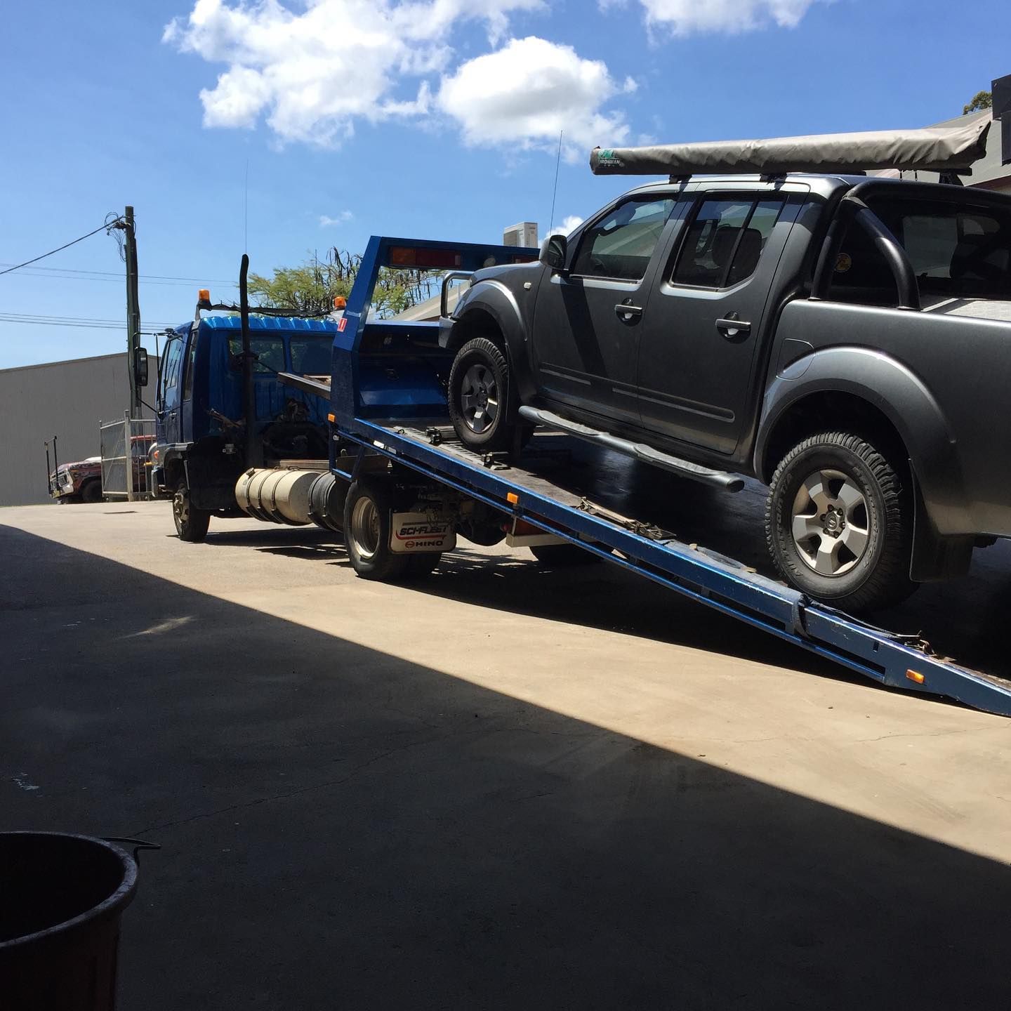 Black pickup truck on a blue tow truck ramp under a sunny sky in an industrial lot — Bangalow Towing in Bangalow, NSW