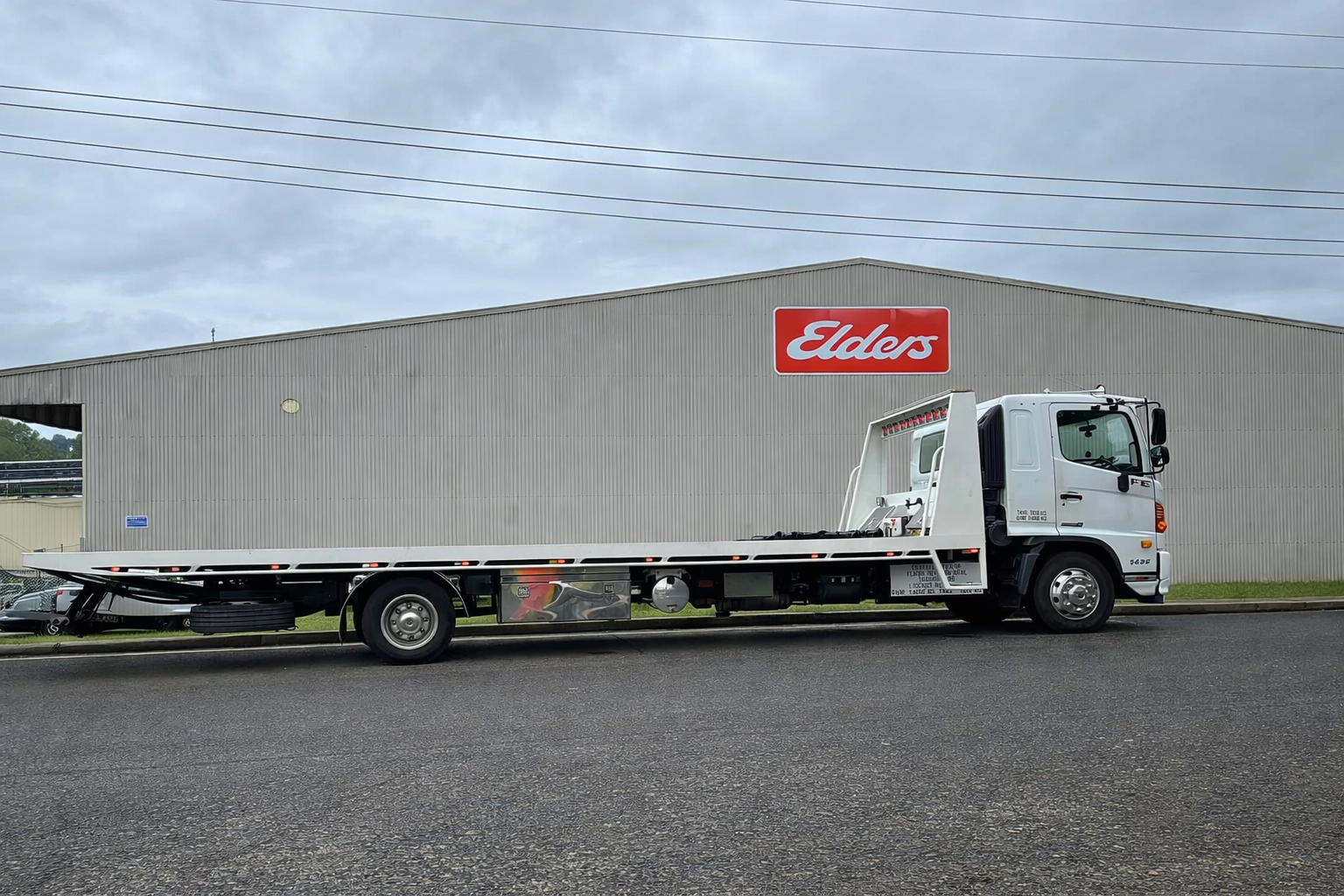 White flatbed truck parked beside a gray Eddis warehouse on a cloudy day — Bangalow Towing in Bangalow, NSW