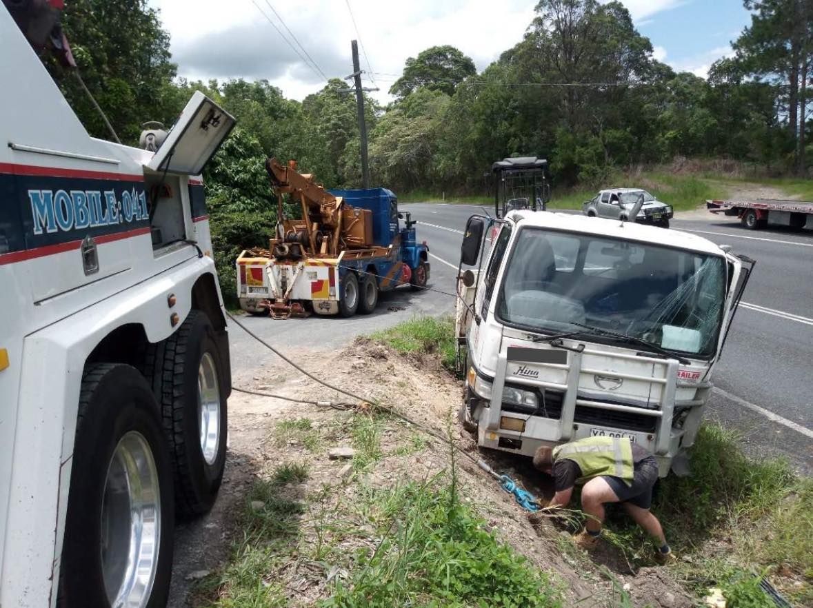 Tow trucks pulling a damaged truck from a roadside ditch. A person works on the damaged truck — Bangalow Towing in Bangalow, NSW