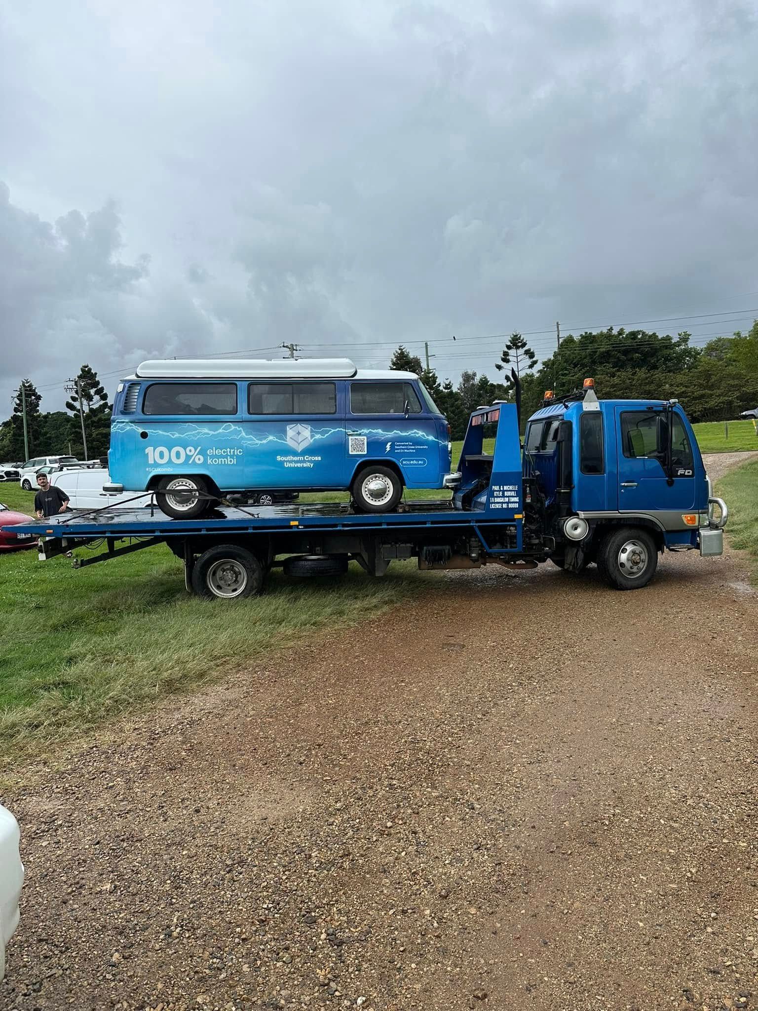 Blue van loaded on a flatbed tow truck in a gravel lot under cloudy skies — Bangalow Towing in Bangalow, NSW