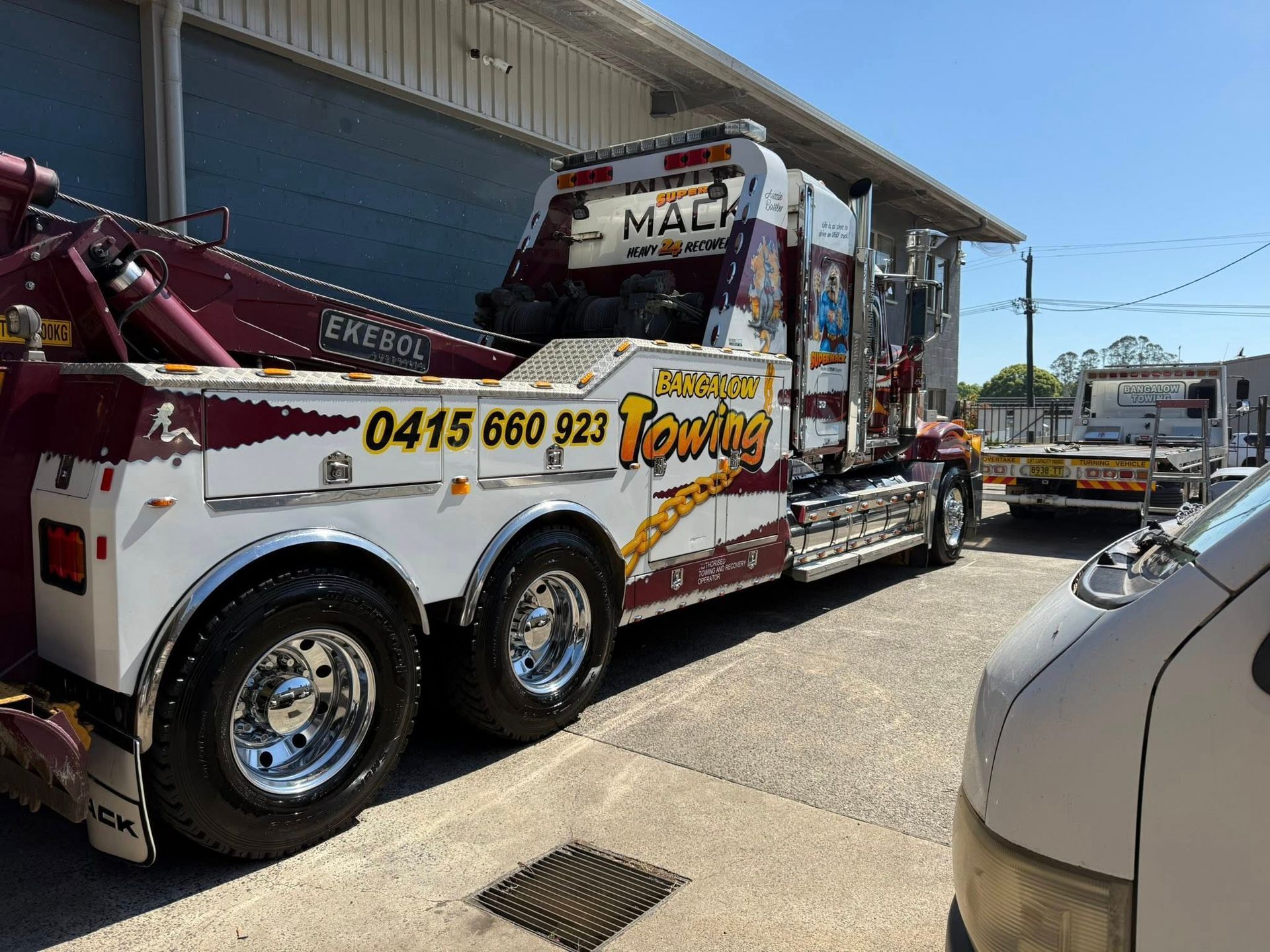 Tow truck parked beside a building, white and red with phone number on the side — Bangalow Towing in Bangalow, NSW