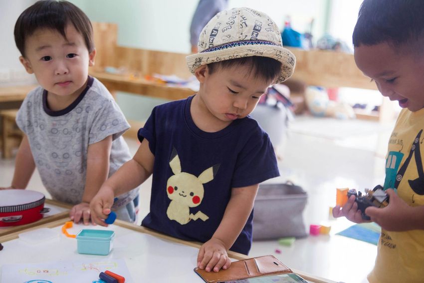Three children playing with toys at a table in a bright classroom