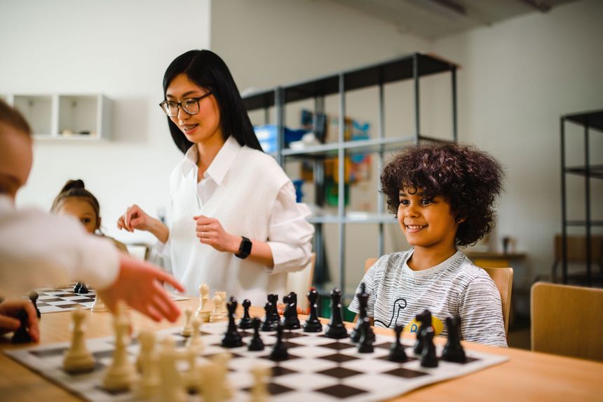 People playing chess at a table, with one person smiling in a bright room