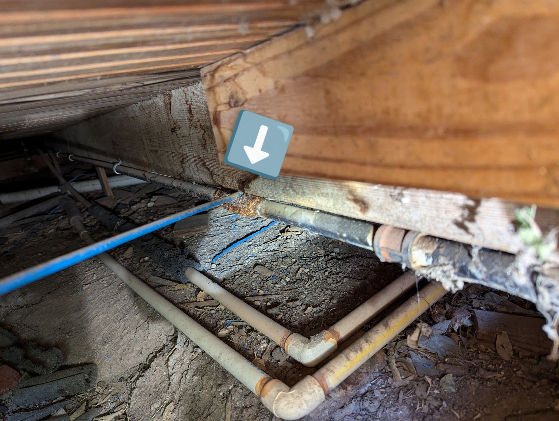 A blue sign with an arrow pointing down is sitting on the ground next to a bunch of pipes.