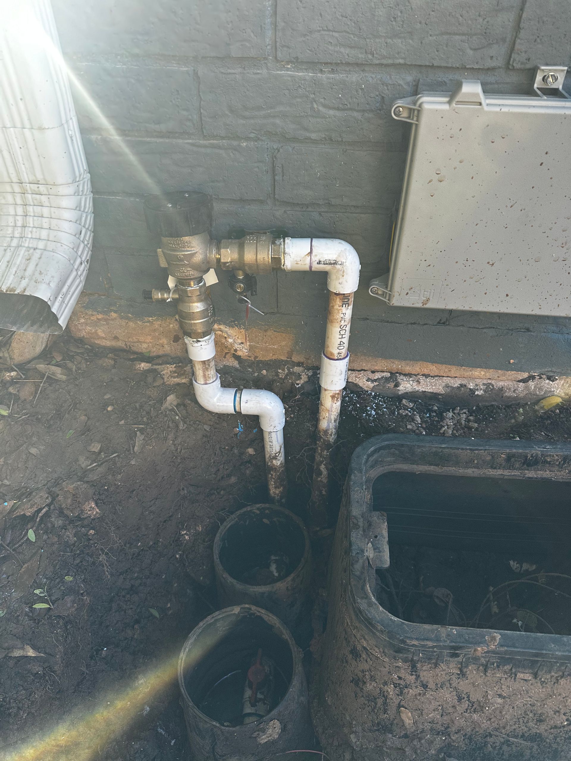 A water pipe is connected to a box on the ground next to a brick wall.