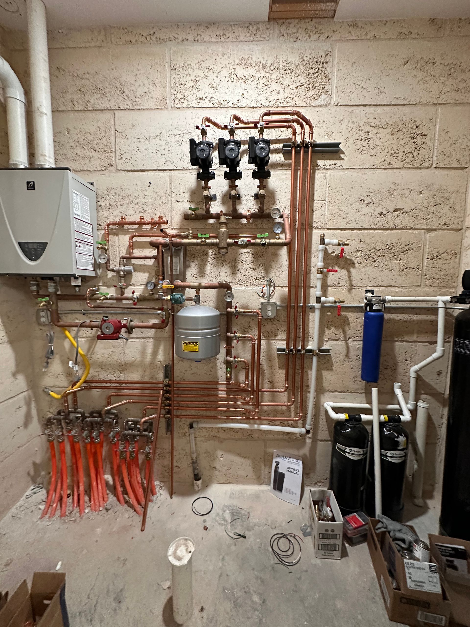 A room with a lot of pipes and a boiler on the wall.