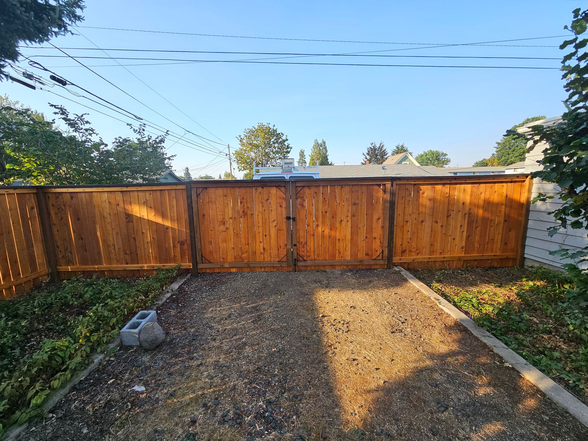 Freshly landscaped house side yard with green grass, black mulch, small shrubs, and a yellow wheelbarrow near the wall