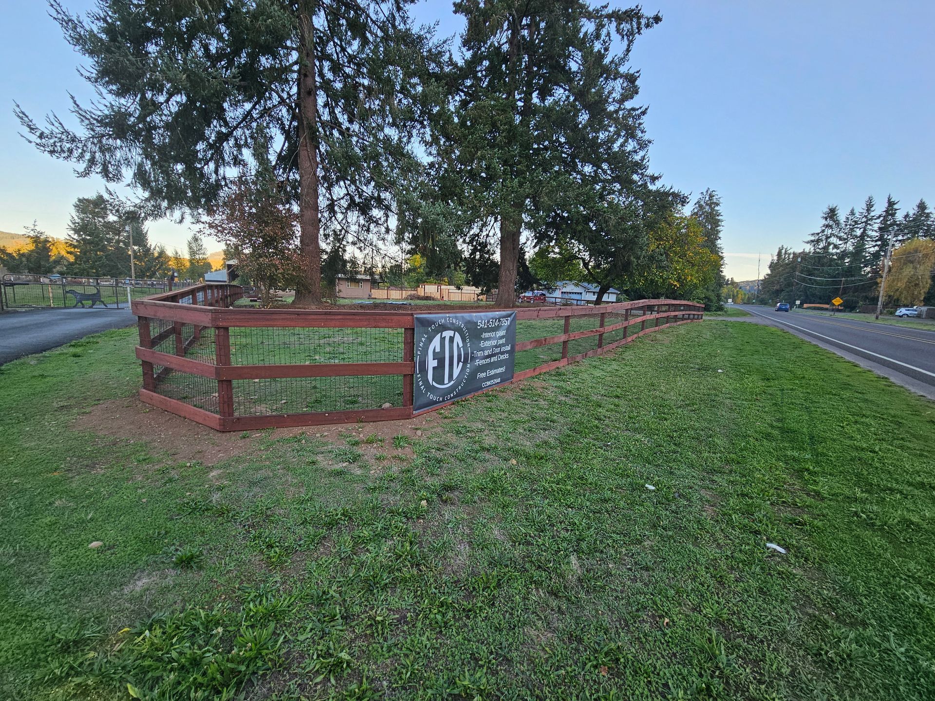 Backyard fence with wooden panels, a small tree, and tall green shrubs under a clear blue sky