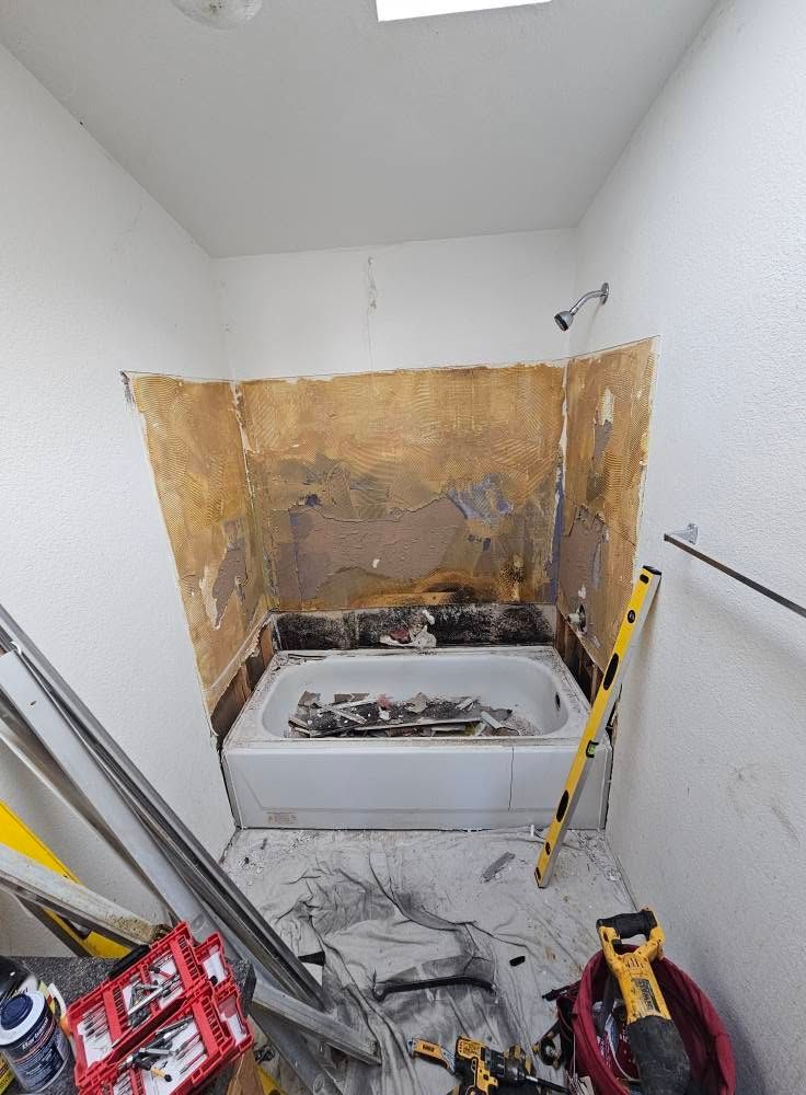 Small bathroom under demolition, with a bathtub, exposed wall behind it, and renovation tools on the floor