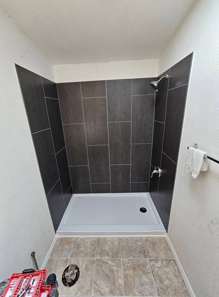 Empty tiled shower stall with white base, dark gray walls, and beige tile floor entry.