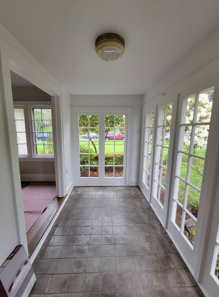 Enclosed porch with tiled floor, white walls, and windows and glass doors overlooking a yard.