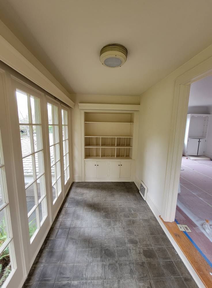 Narrow sunroom with windows, carpet runner, built-in shelves, and doorway to a room beyond.