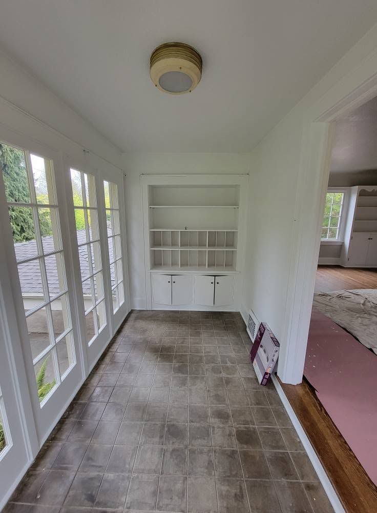 Bright sunroom with French doors, built-in shelves, and a tiled floor; doorway leads to a carpeted room.