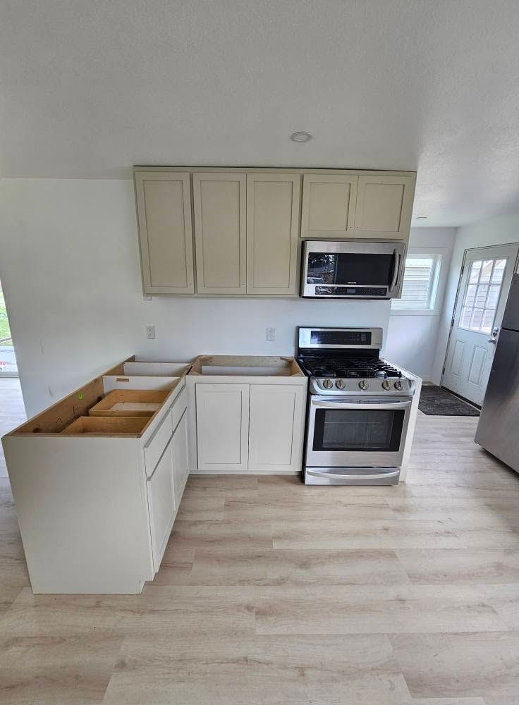 Kitchen with cream cabinets, white appliances, and light wood flooring; one lower cabinet is open.