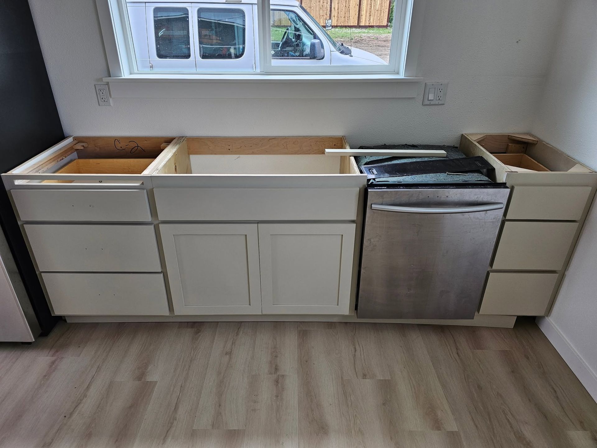 Partially installed kitchen cabinets under a window, with a sink base and dishwasher opening.
