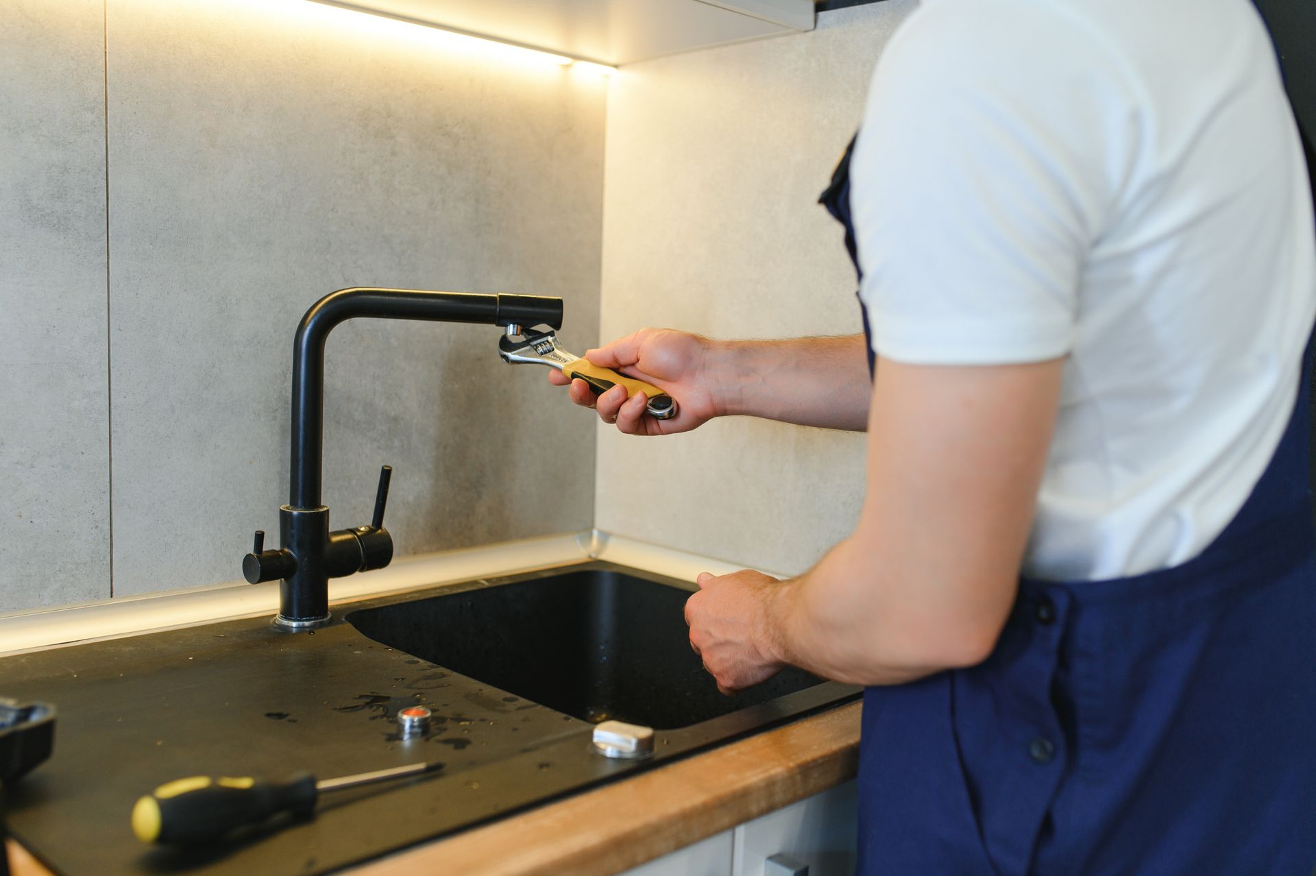 Un homme répare un robinet dans une cuisine avec une clé.