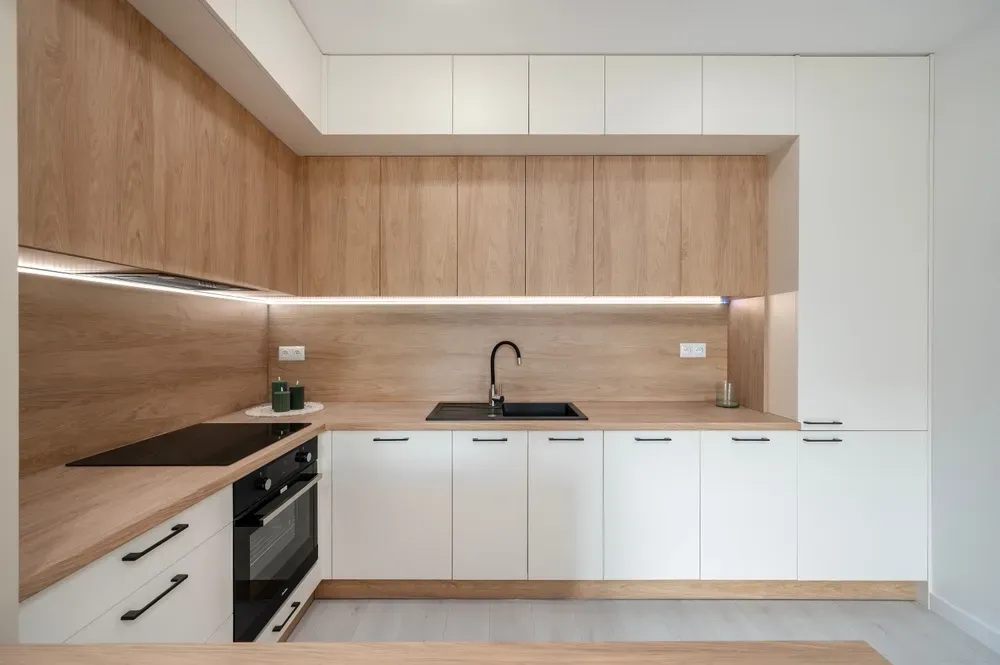 Modern kitchen with white and wood cabinets, black appliances, and countertop lighting. — Dimond J Carpentry in Nambour, QLD