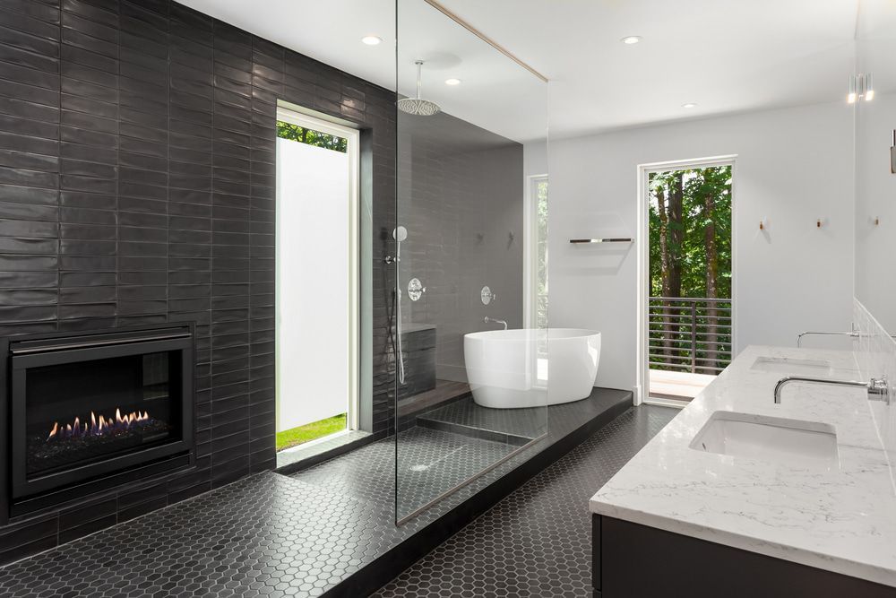 Modern bathroom with black tiled walls, fireplace, walk-in shower, and white soaking tub. — Dimond J Carpentry in Nambour, QLD