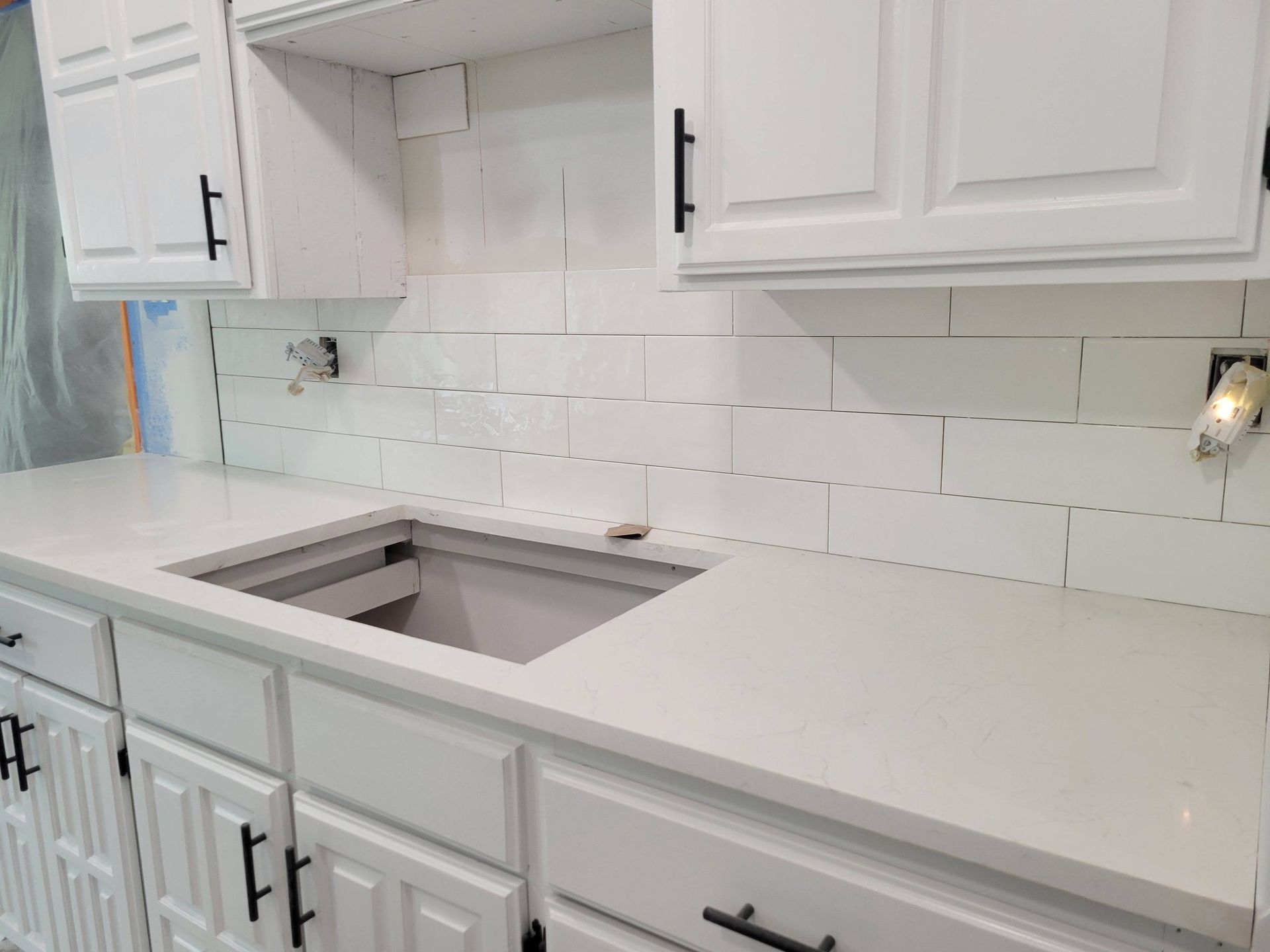 White kitchen with cabinets, subway tile backsplash, and a light countertop with sink cutout