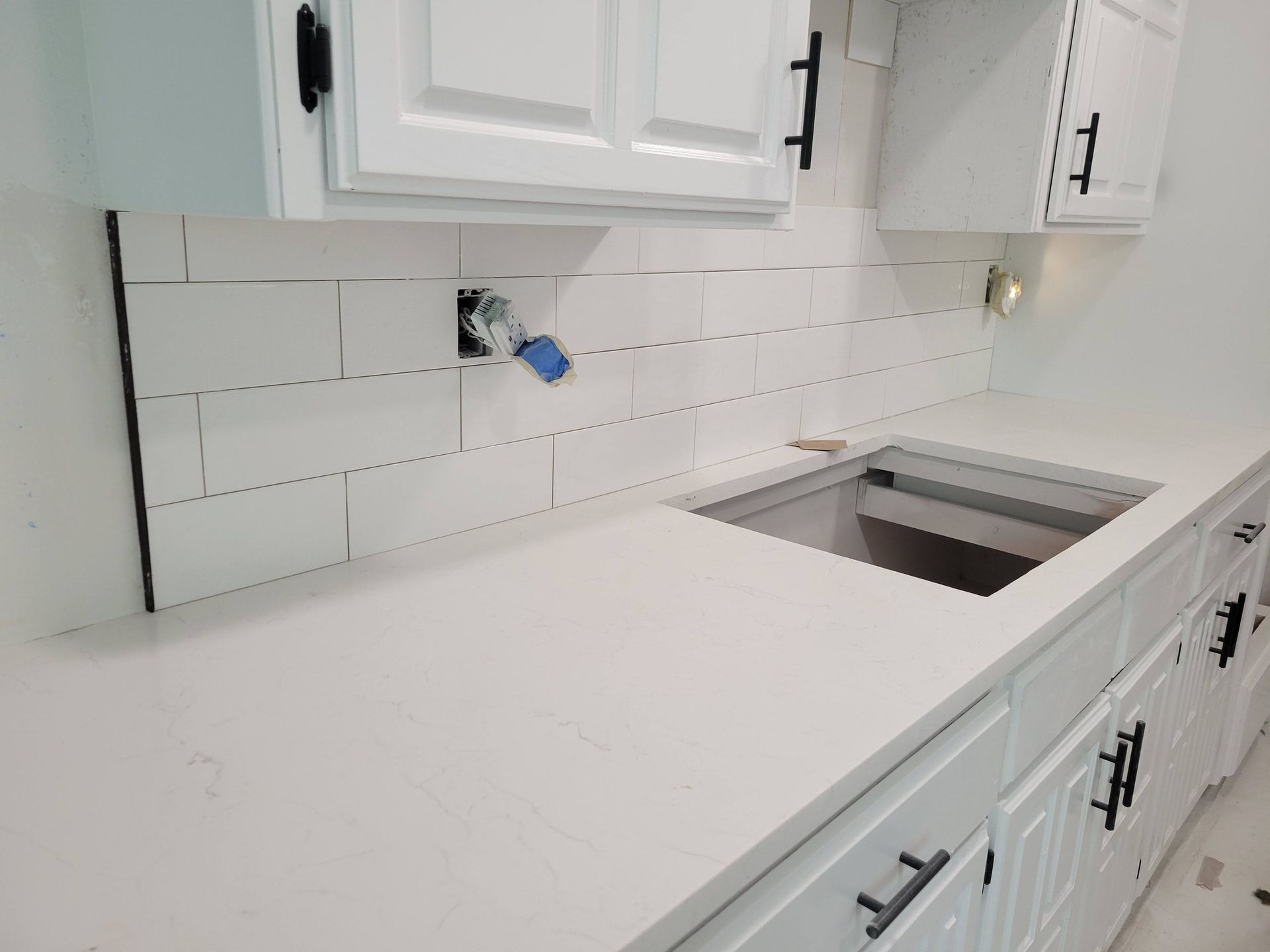 White kitchen countertop with white cabinets, tiled backsplash, and an inset sink on the right.
