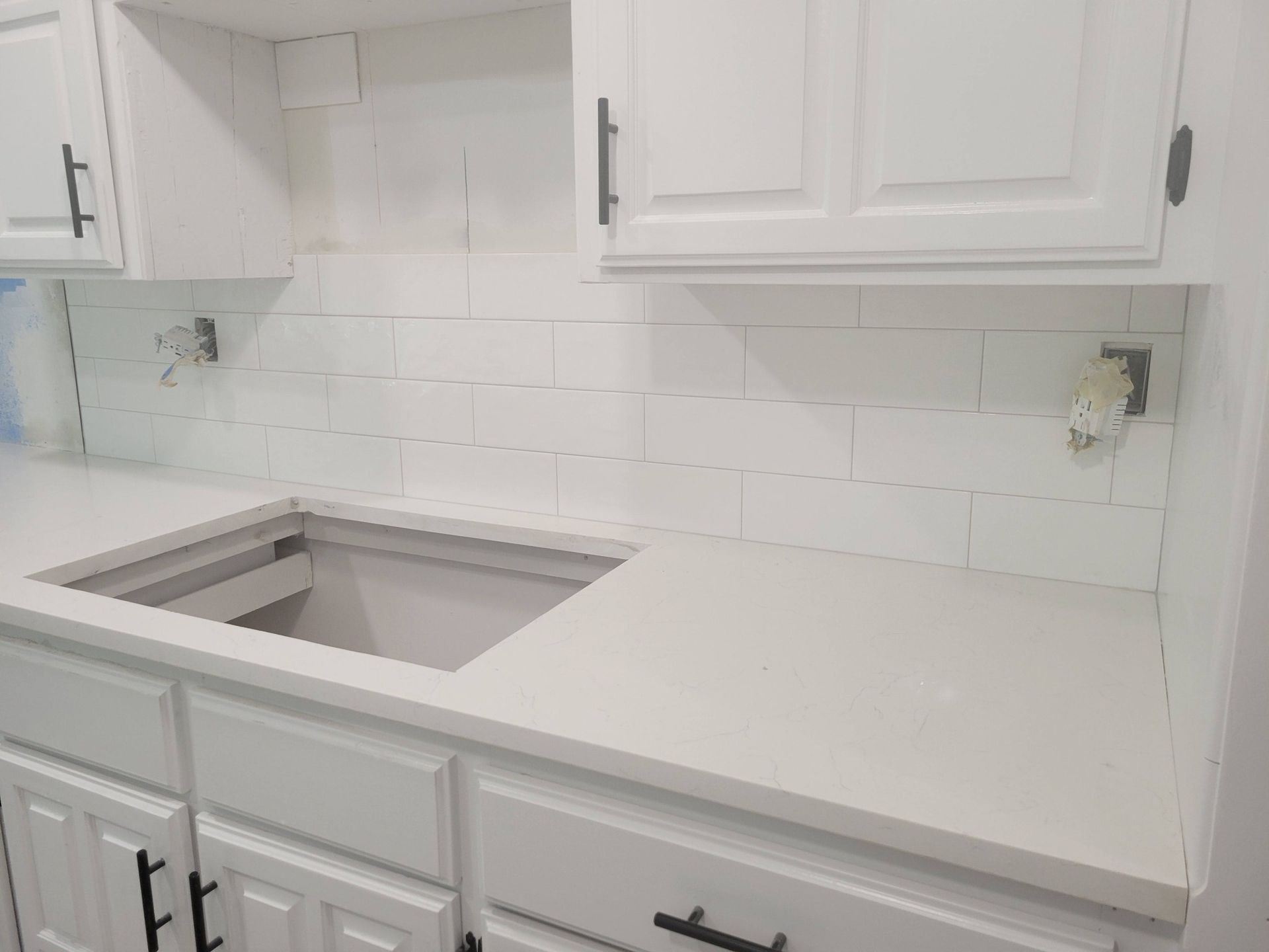 White kitchen countertop with undermount sink, tile backsplash, and upper and lower cabinets