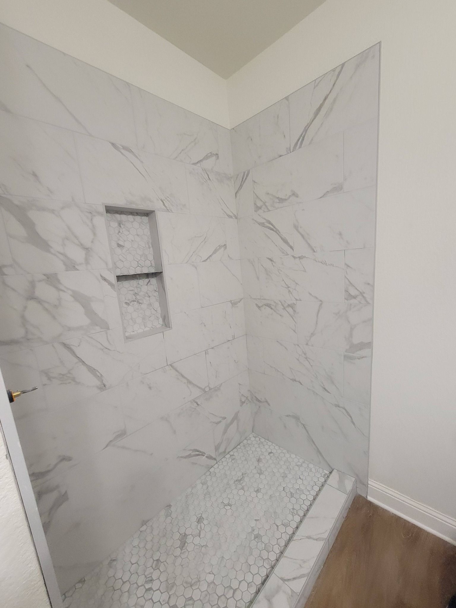 Tiled shower stall with marble-look walls, built-in niche, and white pebble shower floor.
