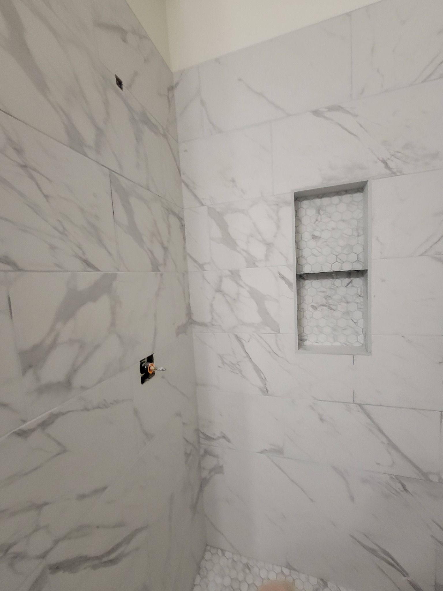 Marble-tiled shower wall with a small recessed niche and unfinished wall opening