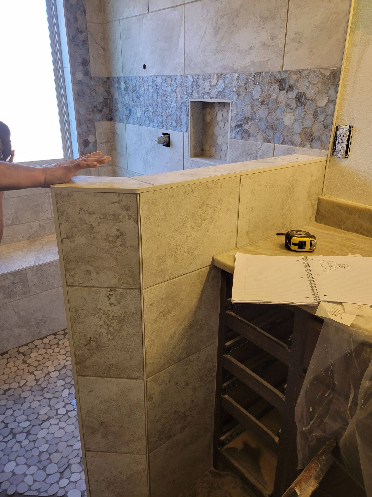 Bathroom vanity under construction with stone tile, a sink cutout, and a person’s arm pointing at it