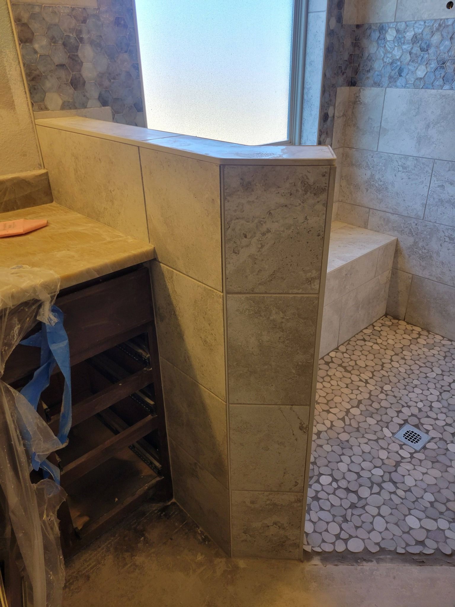 Tiled bathroom with a shower bench, window ledge, and mosaic floor.