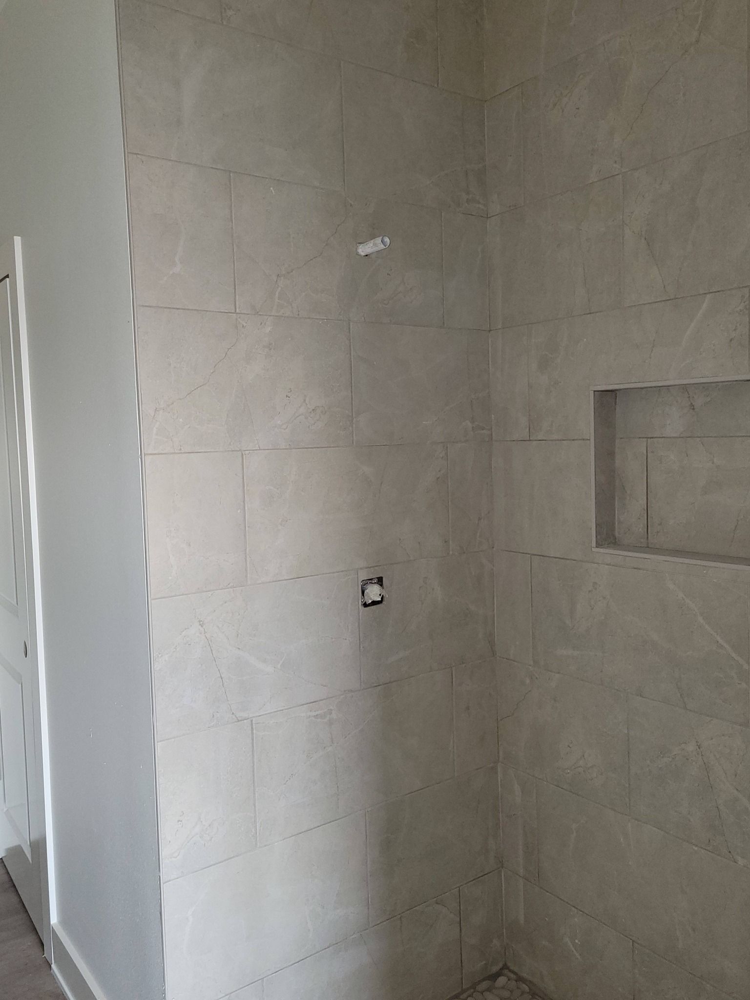 Unfinished tiled bathroom wall with electrical outlet and recessed shelf opening