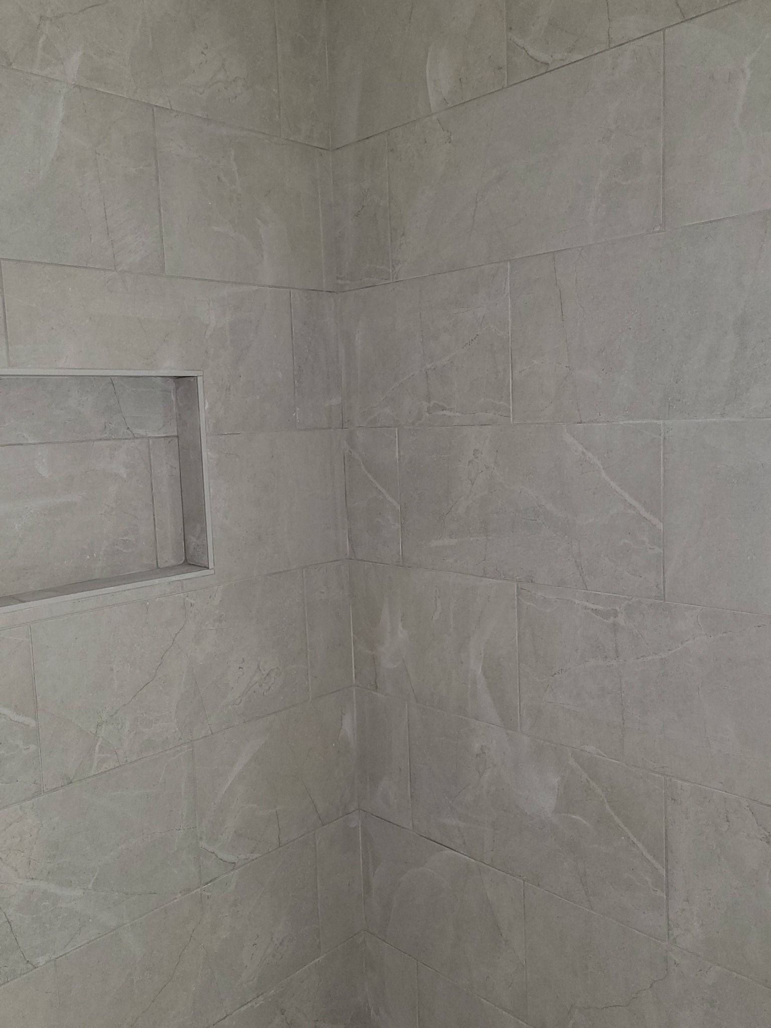 Gray tiled shower wall with a recessed niche.
