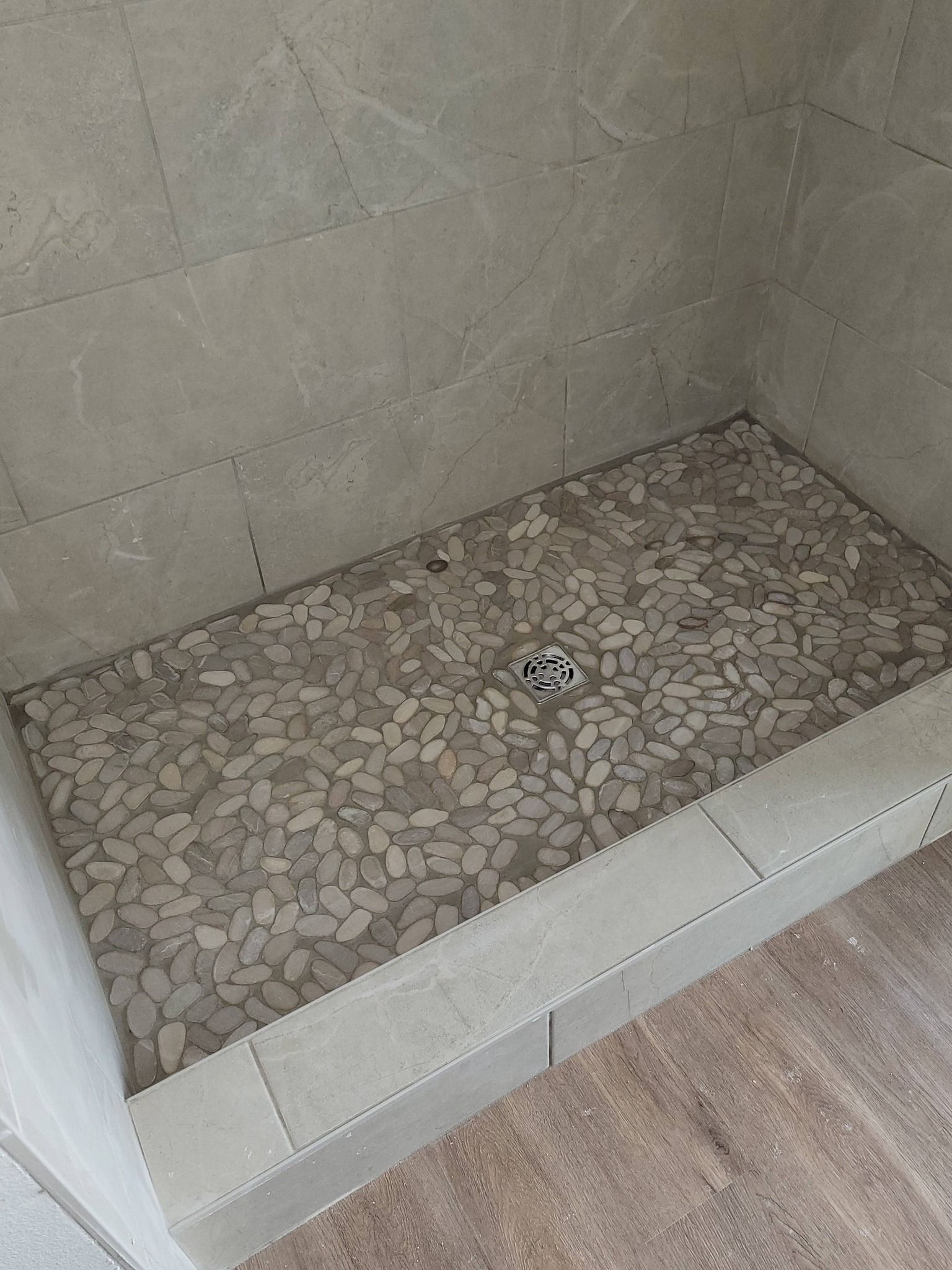 Stone-tiled shower floor with a small drain in a tiled corner.