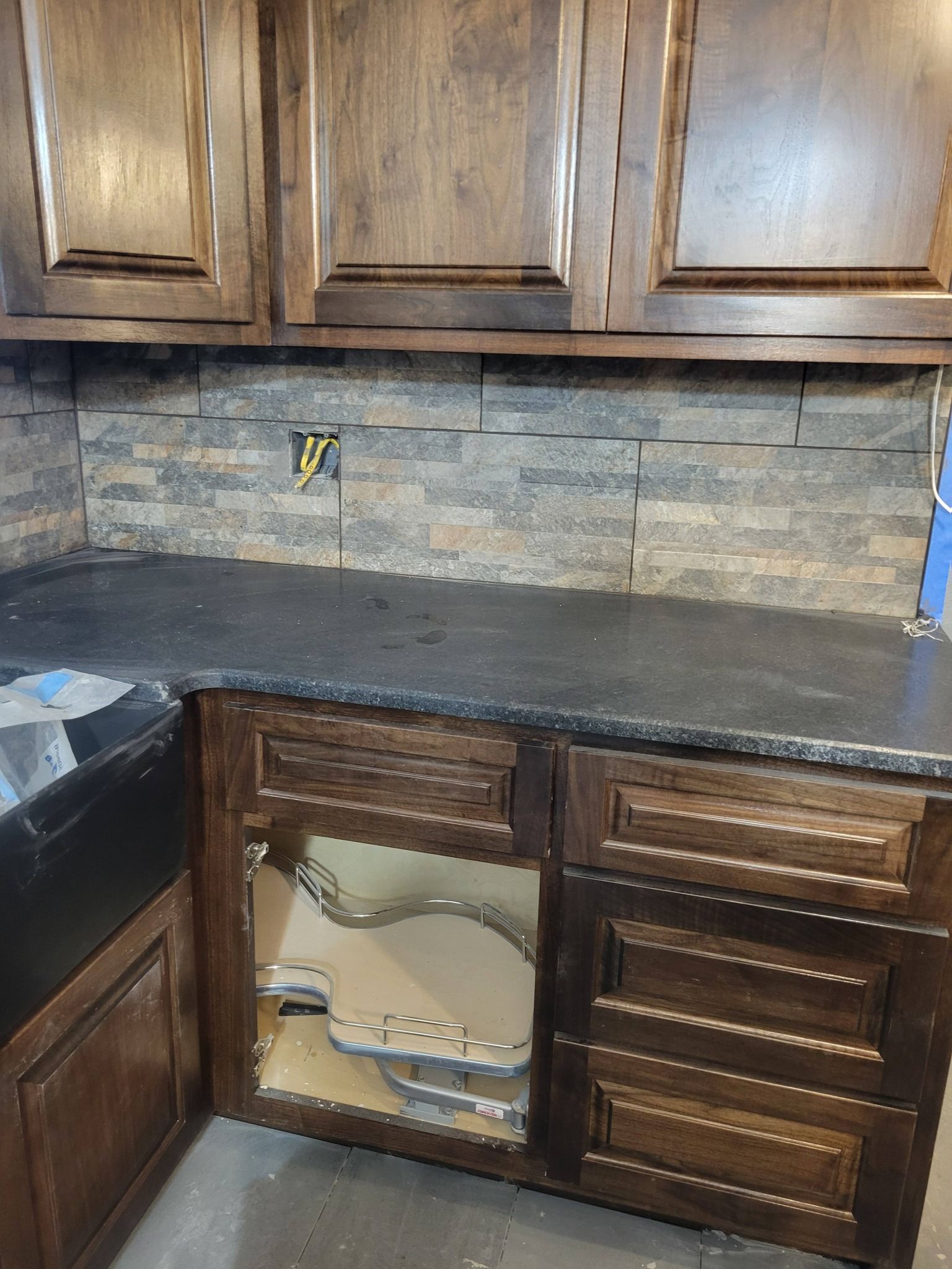 Kitchen counter with dark wood cabinets, stone backsplash, and a sink area under renovation.