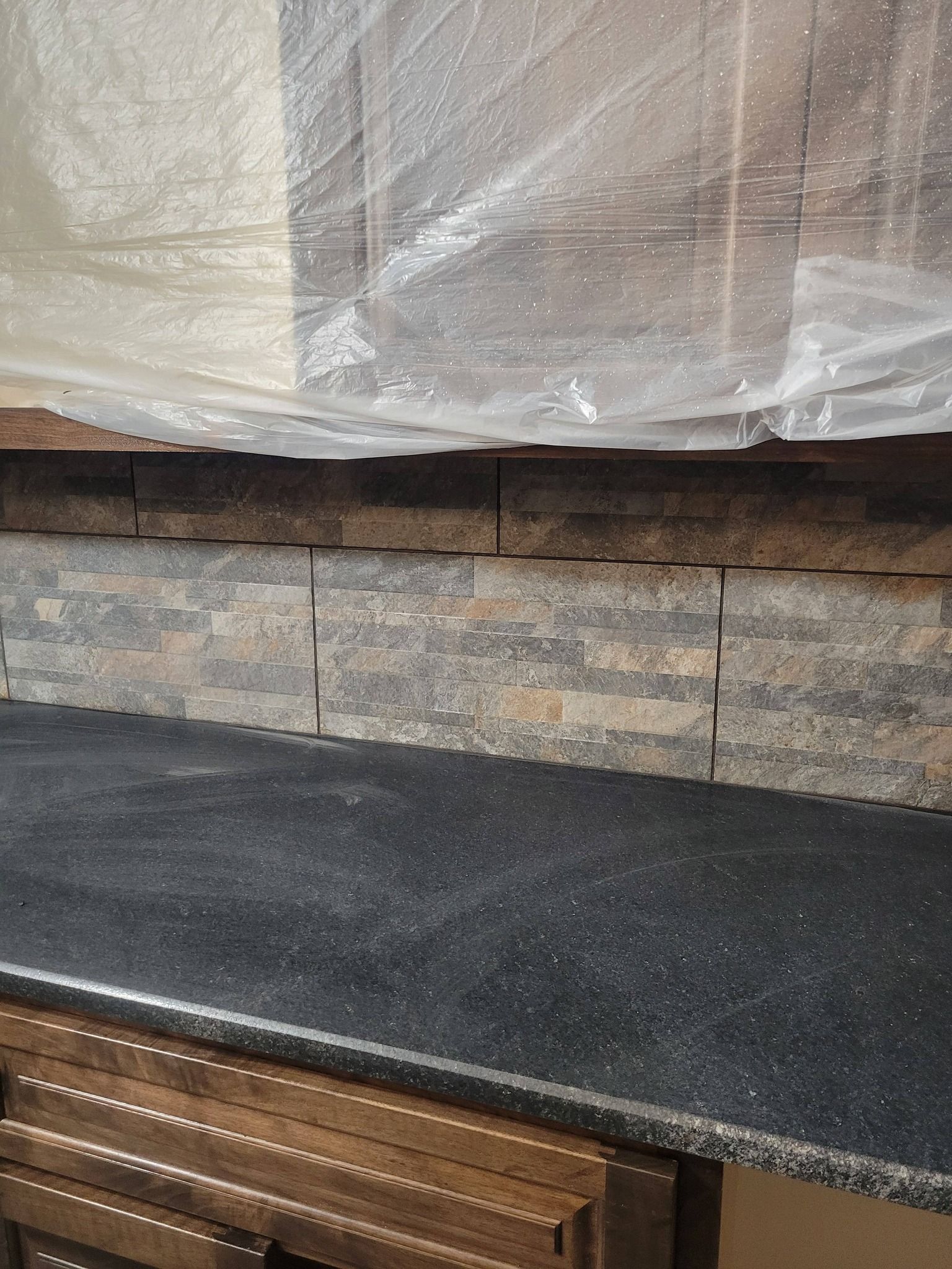 Black countertop with stone backsplash and plastic-covered upper cabinets in a kitchen remodel.