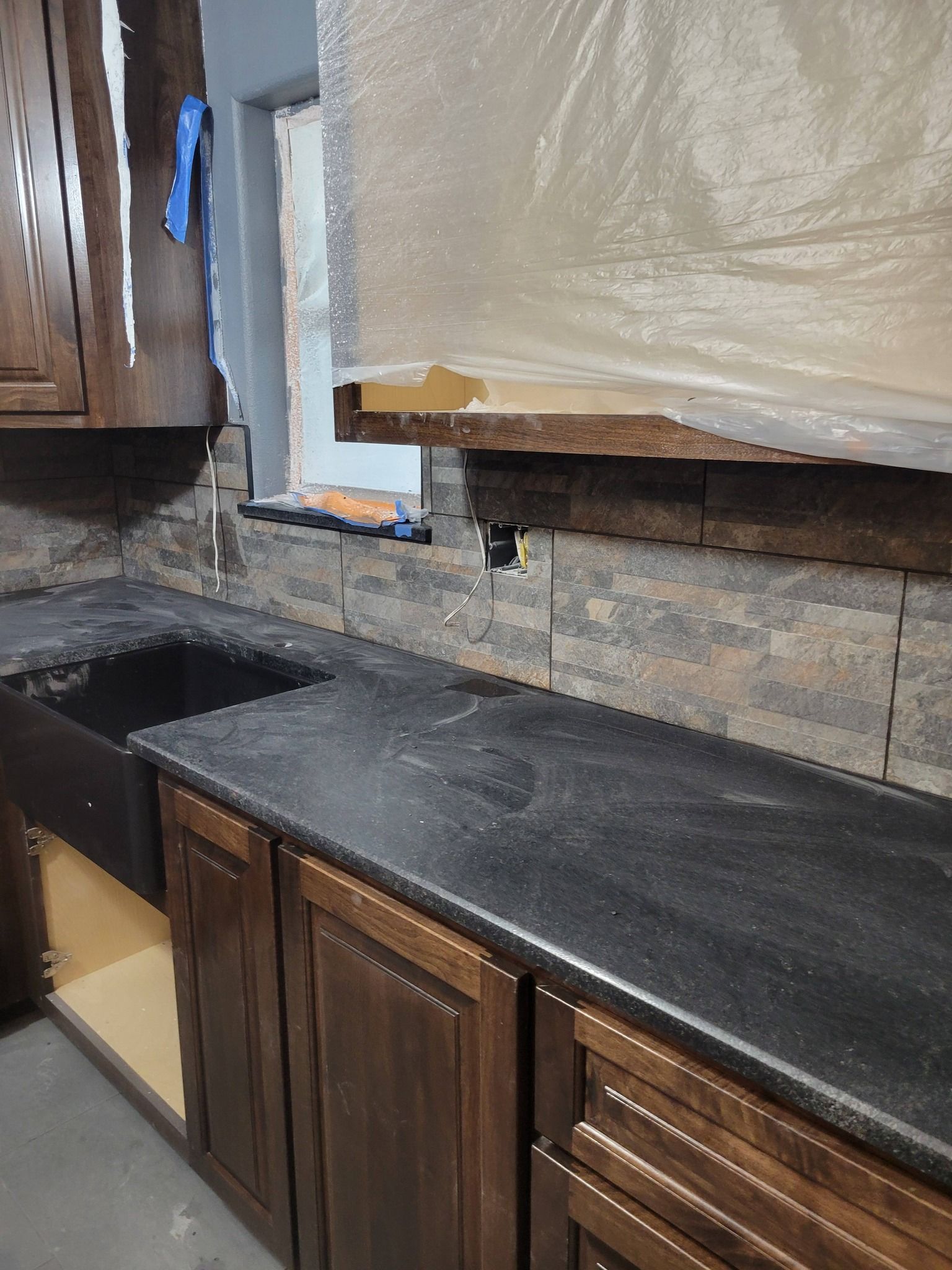 Kitchen countertop with sink, cabinet doors, and a plastic-covered backsplash under renovation