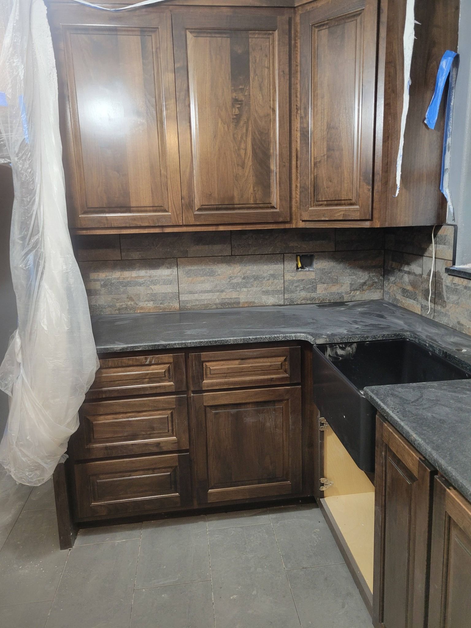 Dark wood kitchen cabinets and counters with a gray backsplash and unfinished lower cabinet area