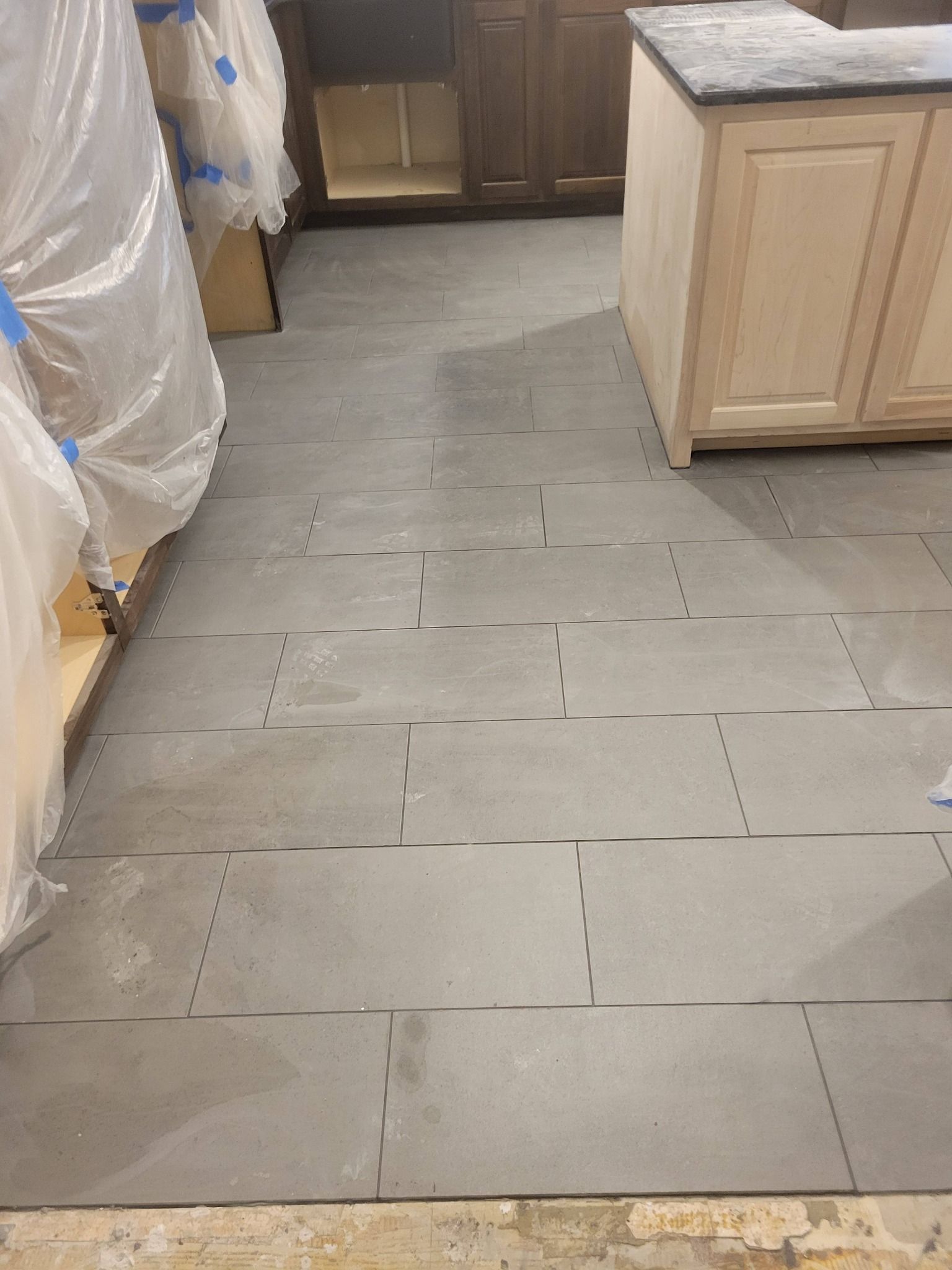 Kitchen floor under renovation with gray square tiles and covered appliances along the sides