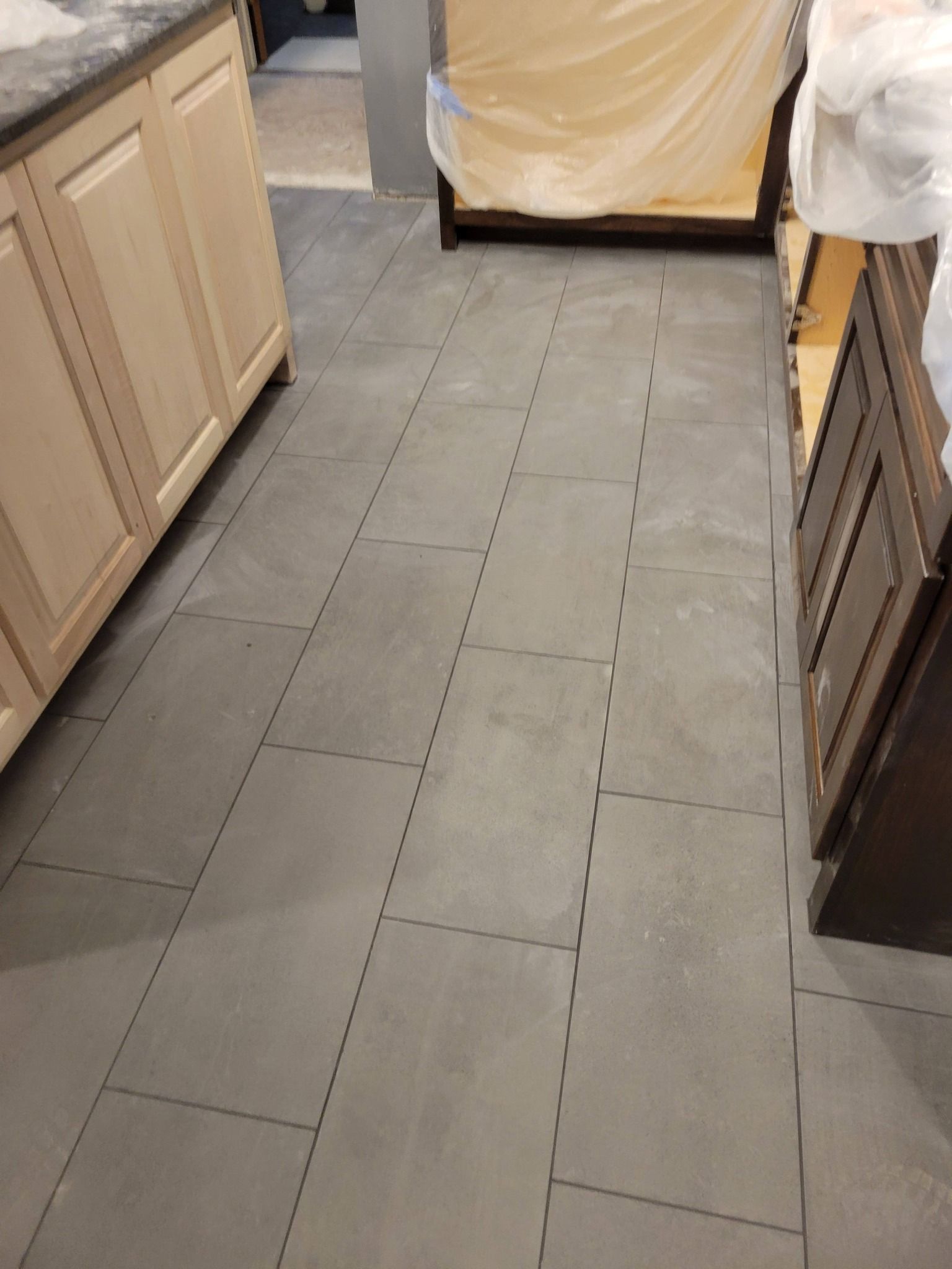 Tiled kitchen floor walkway between cabinets, with furniture covered in protective plastic.