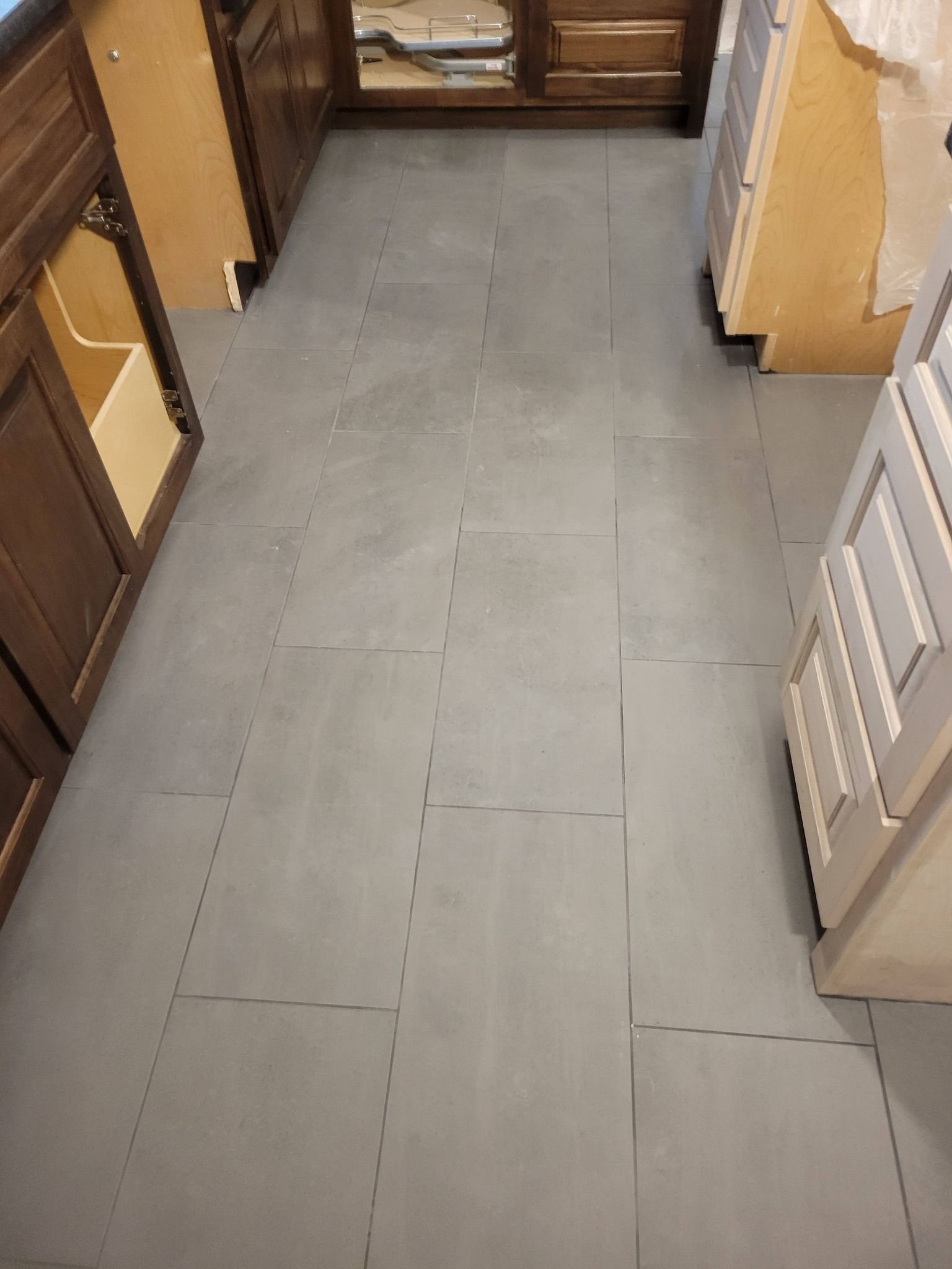 Narrow kitchen aisle with gray tiled floor, wooden cabinets, and a white radiator on the right.