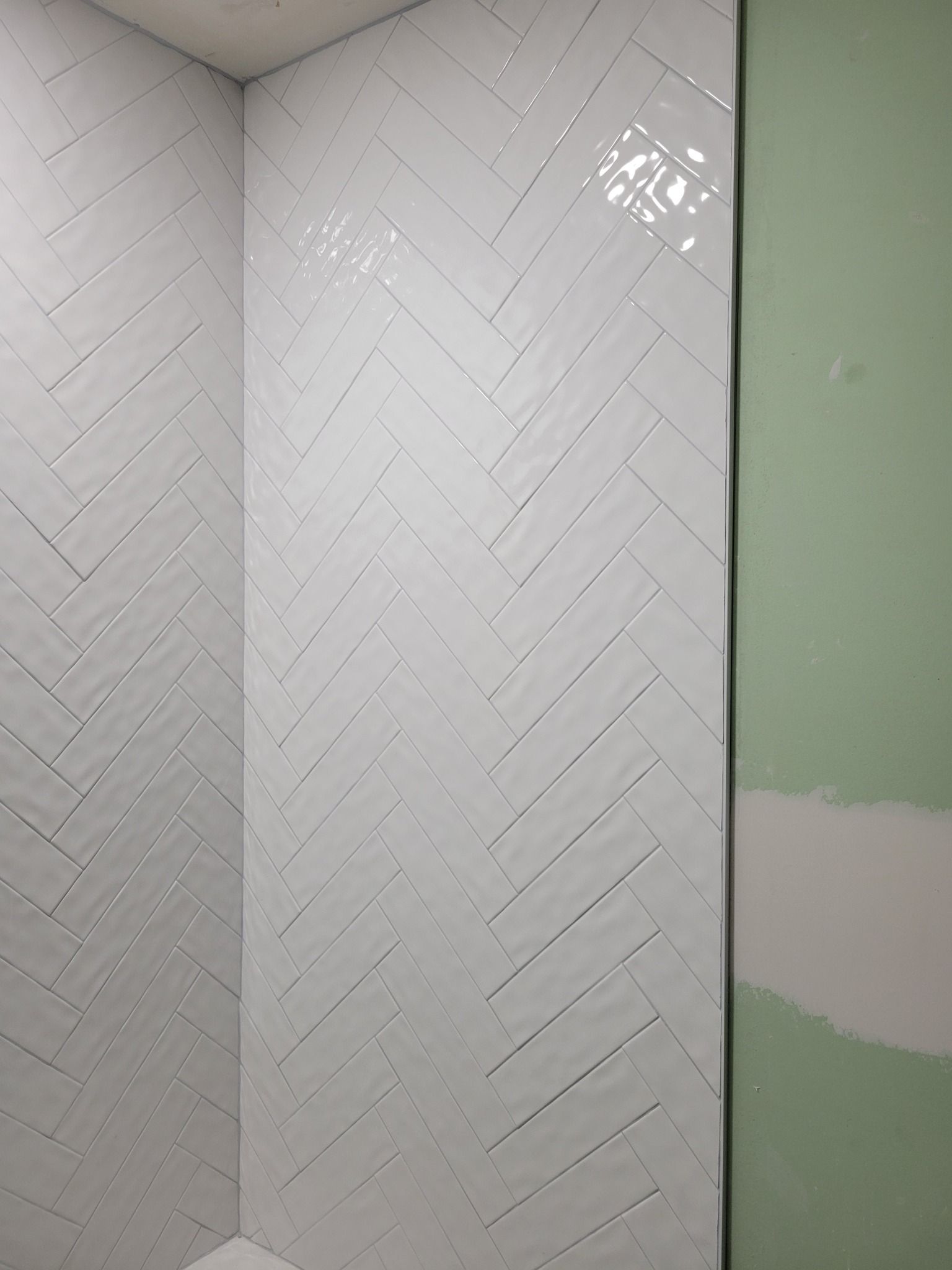 White herringbone-tile shower corner beside a partially painted light green wall.