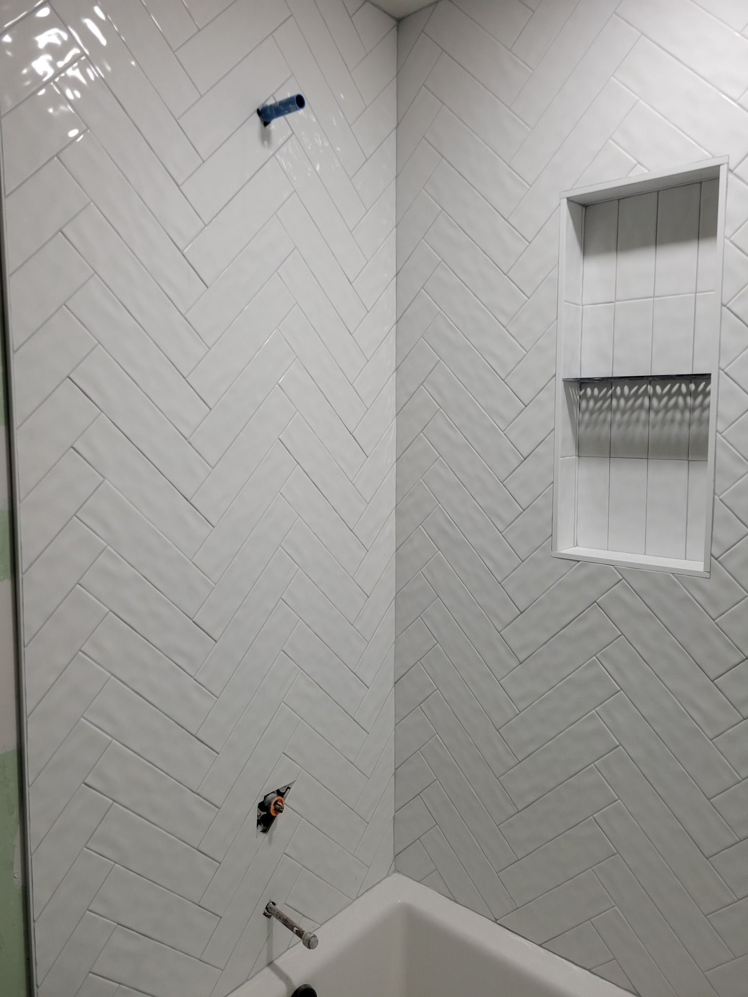 Empty tiled shower with a built-in shelf and a showerhead on the wall.