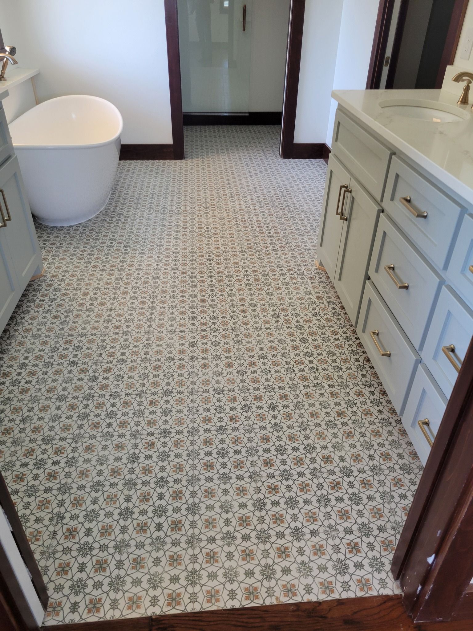 Bathroom with patterned tile floor, white tub, and light-colored vanity cabinets.