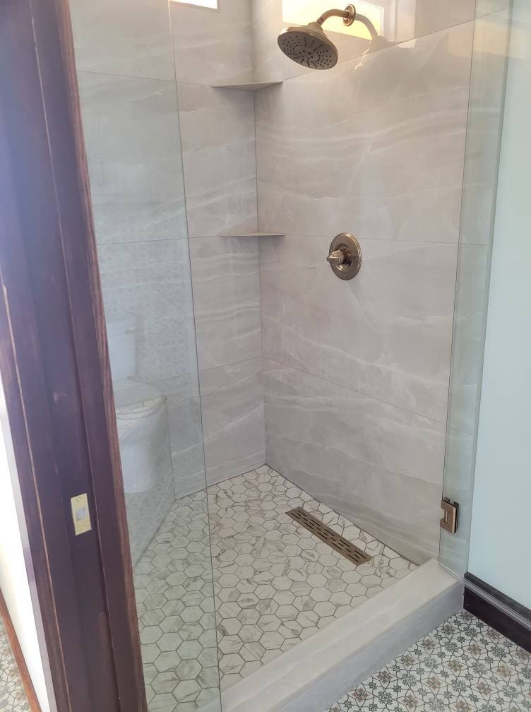 Modern glass shower stall with tiled walls, rain showerhead, and pebble-pattern floor.