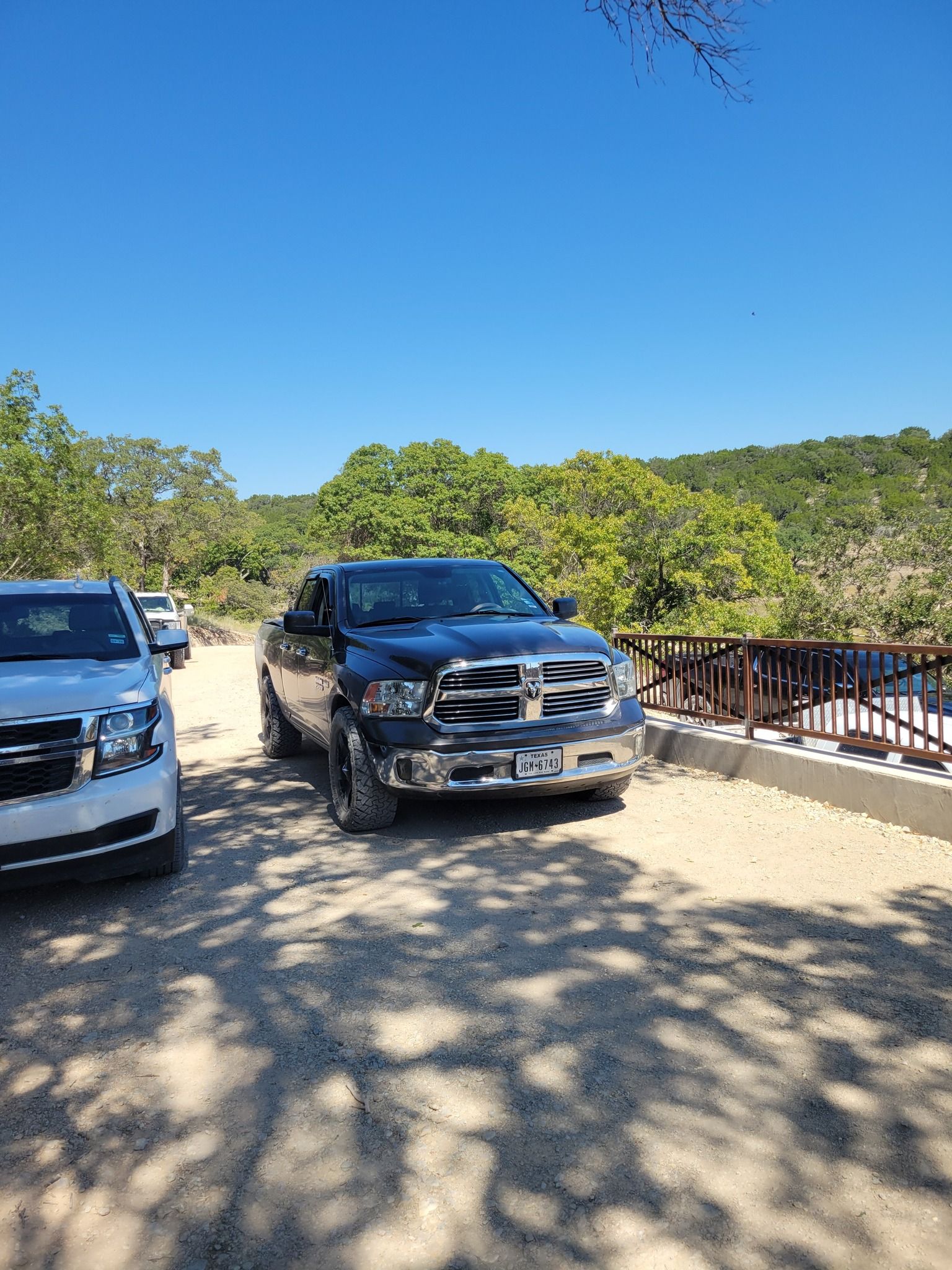 Two parked SUVs on a sunny paved overlook beside a wooden railing and green trees