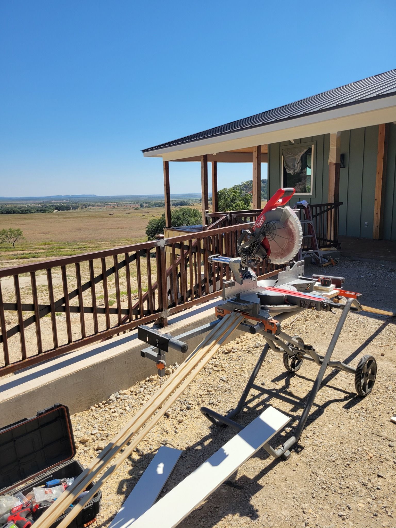 Quilted motor glider parked by a ranch-style porch with a field and hills in the background
