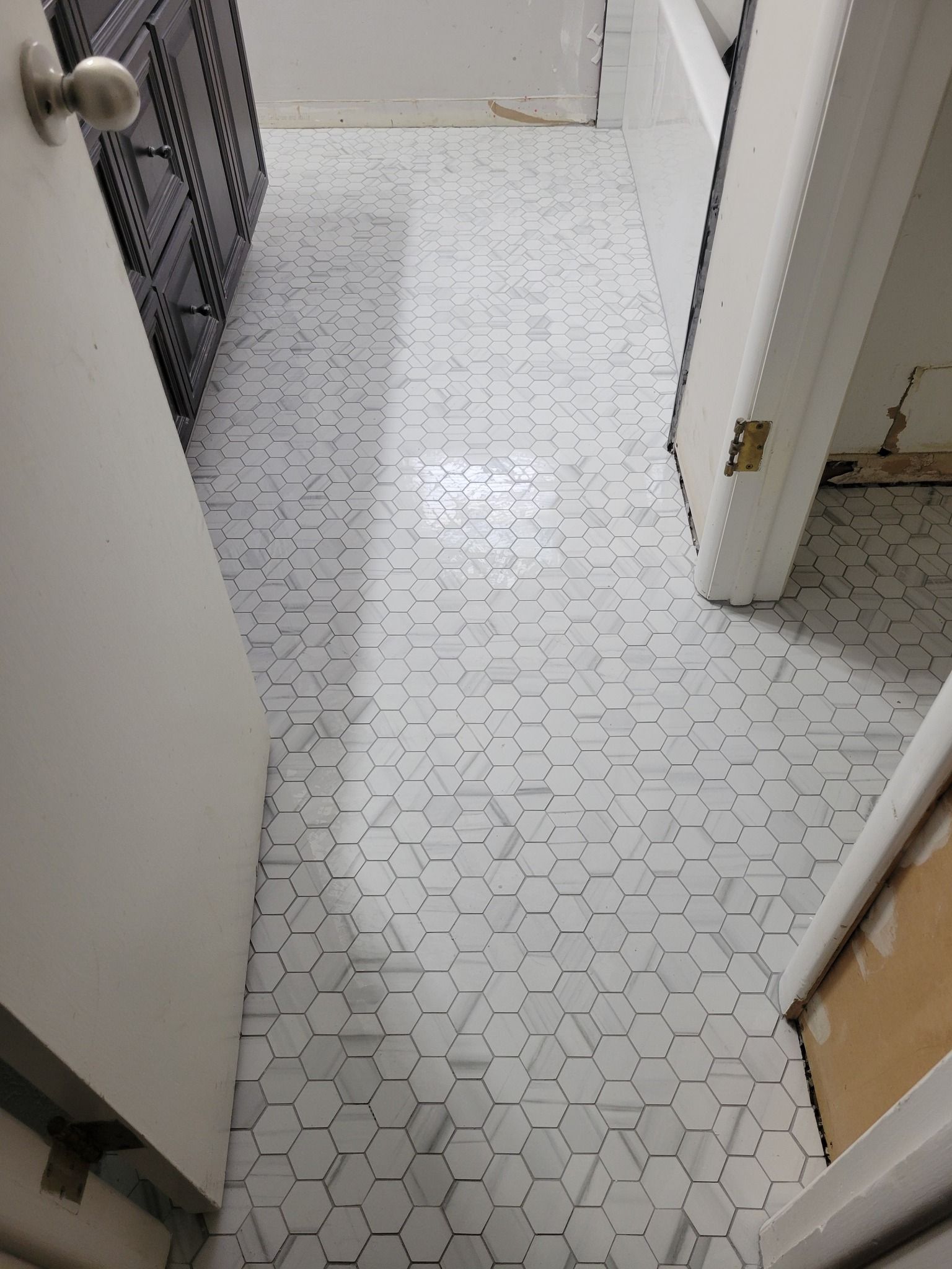 Narrow hallway with white patterned tile floor, open doorways, and a metal gate at left.