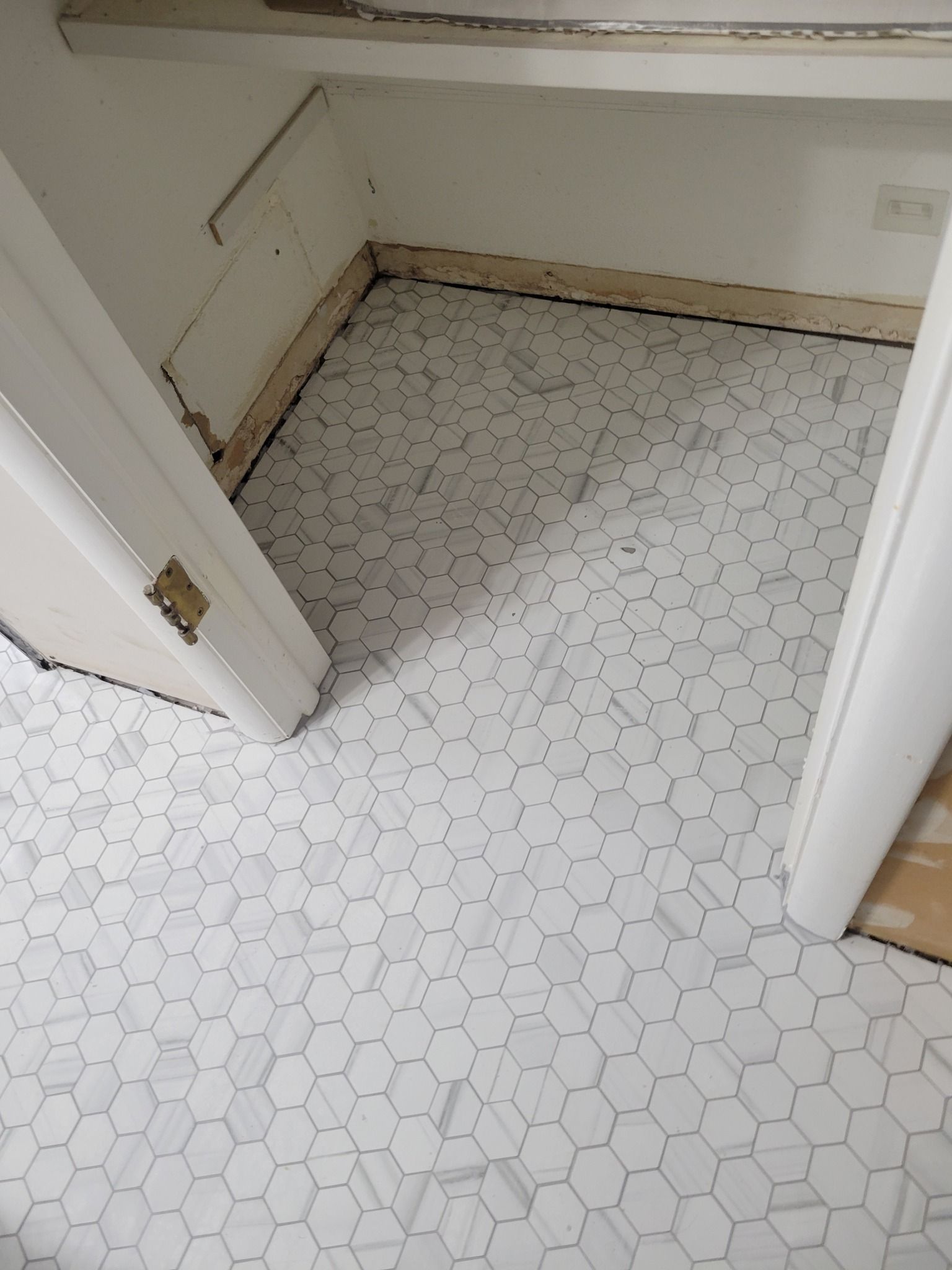 Small empty room with white hexagon tile floor, beige walls, and an open doorway.