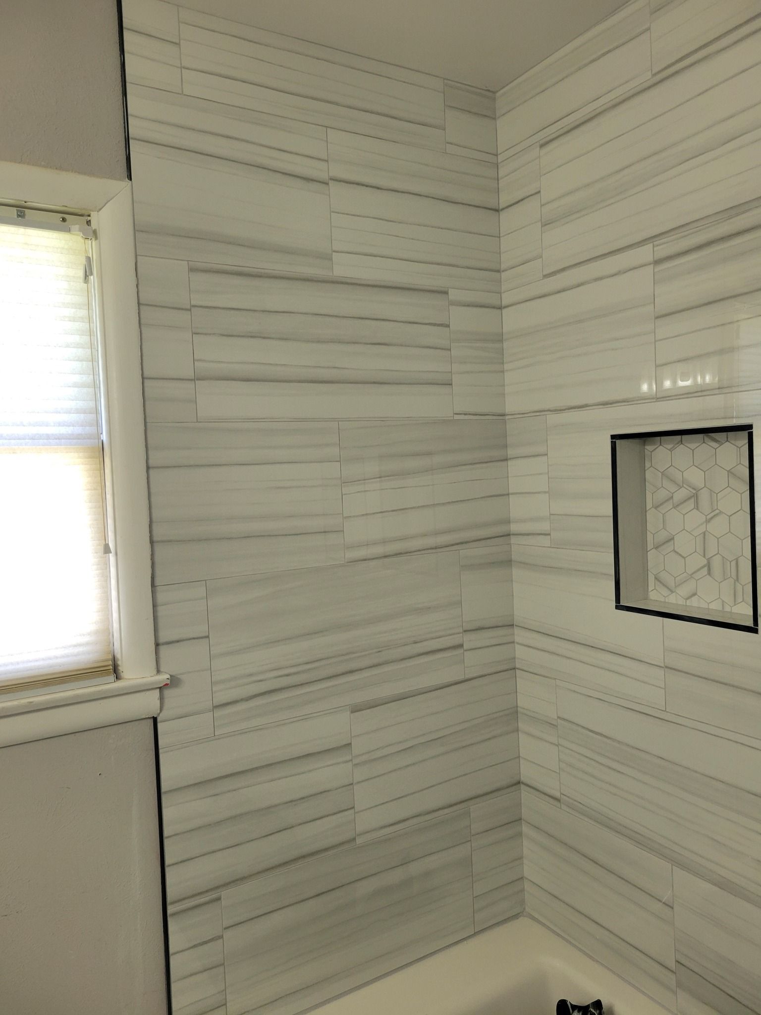 Small bathroom with white plank walls, a window, and a framed mirror above the tub.